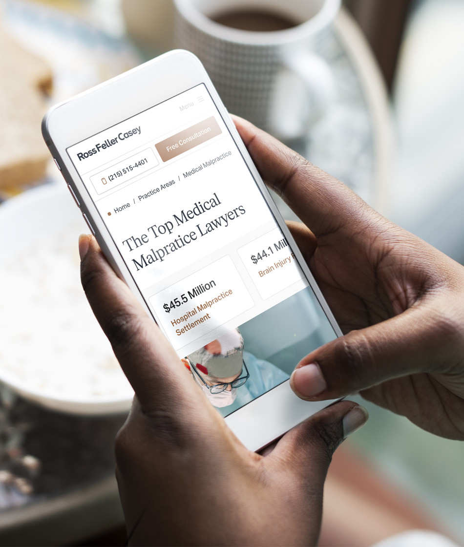 Person holding a smartphone displaying the Ross Feller Casey medical malpractice page with case results including a $45.5 million hospital malpractice settlement