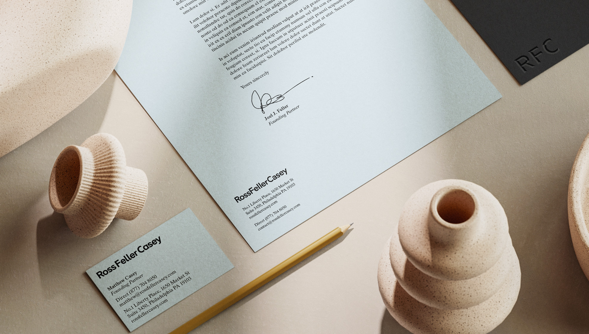 RossFellerCasey branded stationery set displayed on a warm beige surface, including a letterhead and business card. The letterhead features the bold RFC monogram in the upper left corner and the full RossFellerCasey wordmark with contact information at the bottom. A business card is partially visible in the upper right corner.