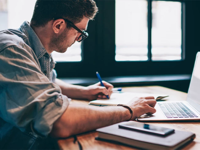 Content marketing strategist writing notes at desk with laptop for law firm digital marketing